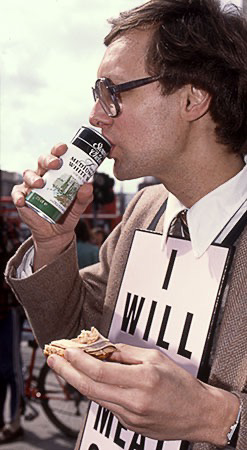 PICTURE: color photo of Gibson holding the uneating half of the meat hors d'oeuvre while at the same time sipping wine from a can.