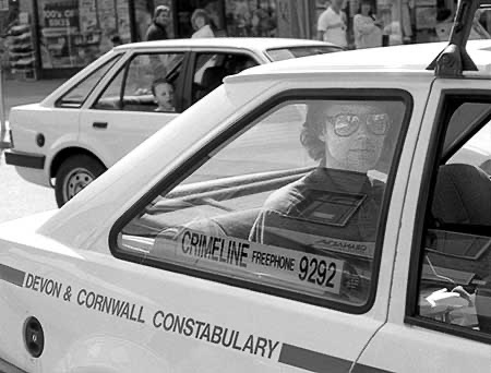 PICTURE: black and white photo of Gibson sitting in the back of the police car and being driven to the police station.