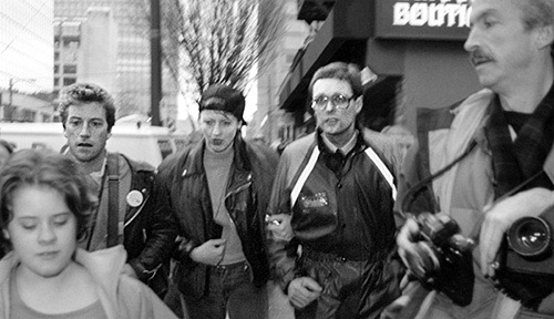 PICTURE: black and white photo of (left to right) Paddy, Susi and Gibson walking with linked arms. 